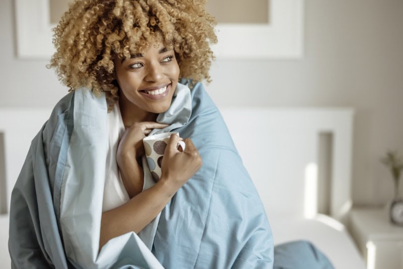 Woman wrapped in blanket enjoying a cup of tea after her furnace maintenance was completed. Air-Ton Heating & AC blog image.